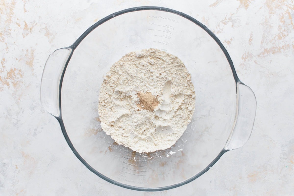 Instant yeast added to gluten-free flour mixture in a glass bowl.
