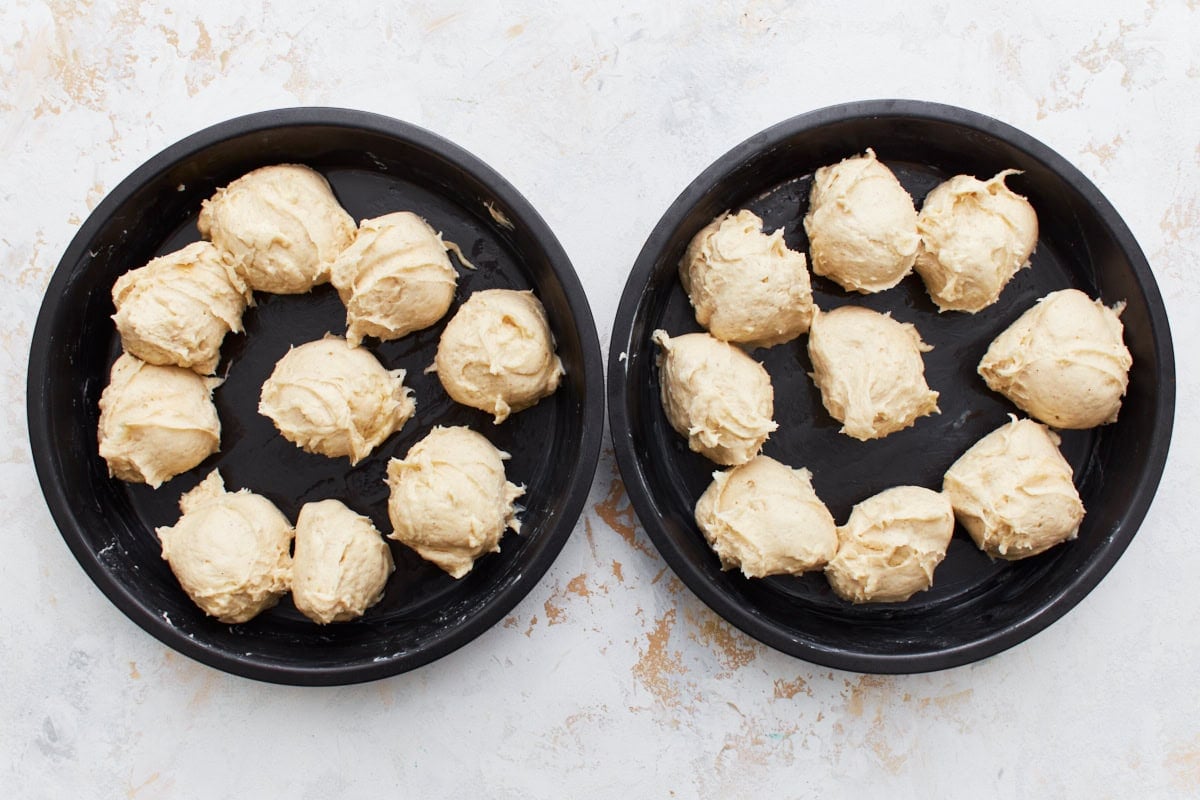 Gluten-free dinner roll dough balls in two cake pans.
