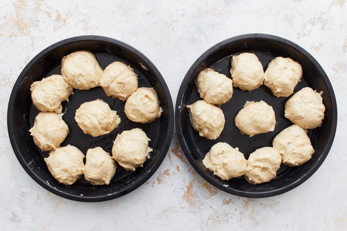 Smoothed gluten-free dinner roll dough balls in two cake pans.