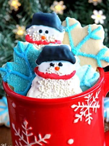 gluten-free sugar cookie cut outs in snow man and snowflakes in a red cup with a Christmas tree in the background