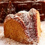 slice of gluten-free gingerbread cake with a gingerbread cake house in the background