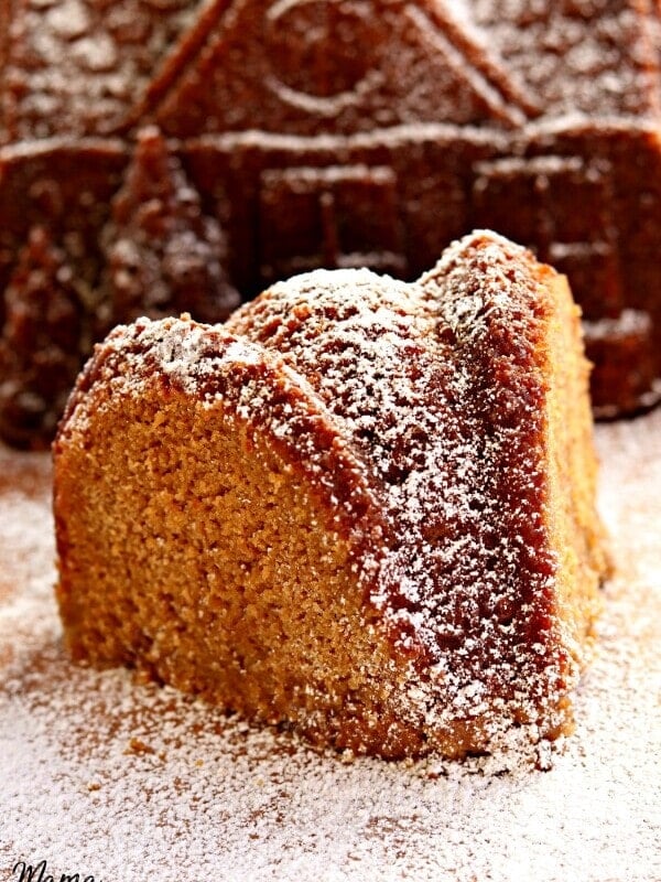 slice of gluten-free gingerbread cake with a gingerbread cake house in the background