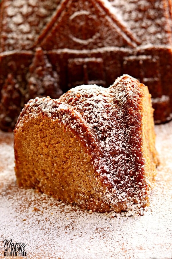 slice of gluten-free gingerbread cake with a gingerbread cake house in the background