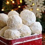 gluten-free snowball cookies in a red cookie tin with a snowflake and lighted tree in the background