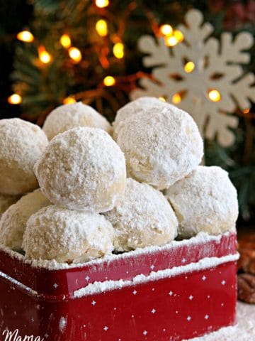 gluten-free snowball cookies in a red cookie tin with a snowflake and lighted tree in the background