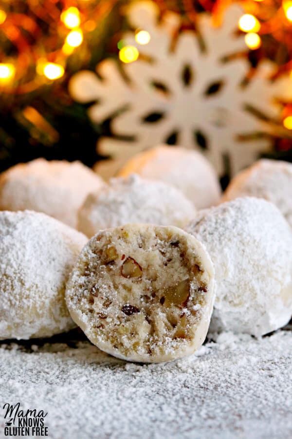 a gluten-free snowball cookie cut in half to show the texture with more cookies and a snowflake and lighted tree in the background