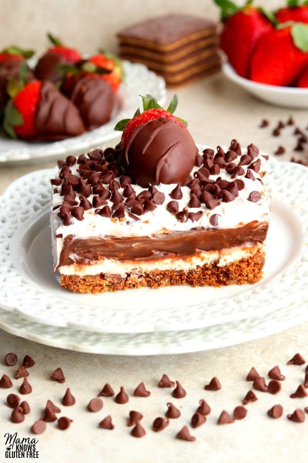 a slice of chocolate lasagna with chocolate covered strawberries, cookies, strawberries and chocolate chips in the background