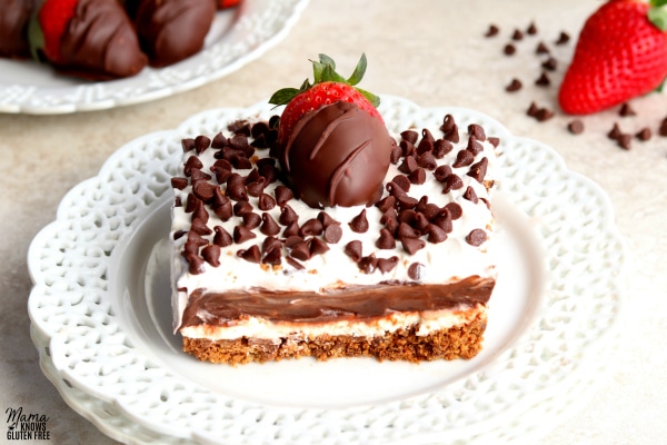 a slice of chocolate lasagna with chocolate covered strawberries, chocolate chips and a strawberry in the background 