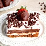 slice of chocolate lasagna with chocolate covered strawberries and chocolate chips in the background