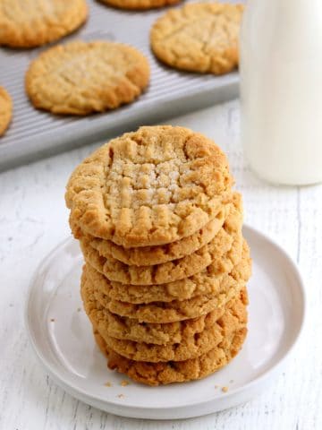 stack of gluten-free peanutbutter cookies with tray of cookies and milk in the background