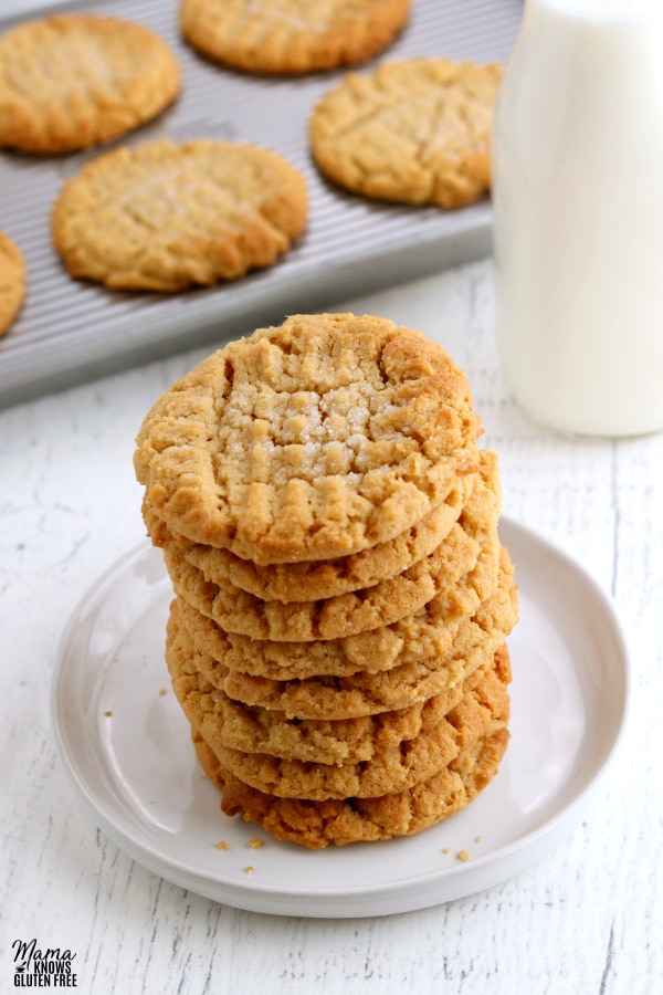stack of gluten-free peanutbutter cookies with tray of cookies and milk in the background