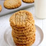 gluten-free peanut butter cookies stacked on a white plate with cookie sheet and milk in the background