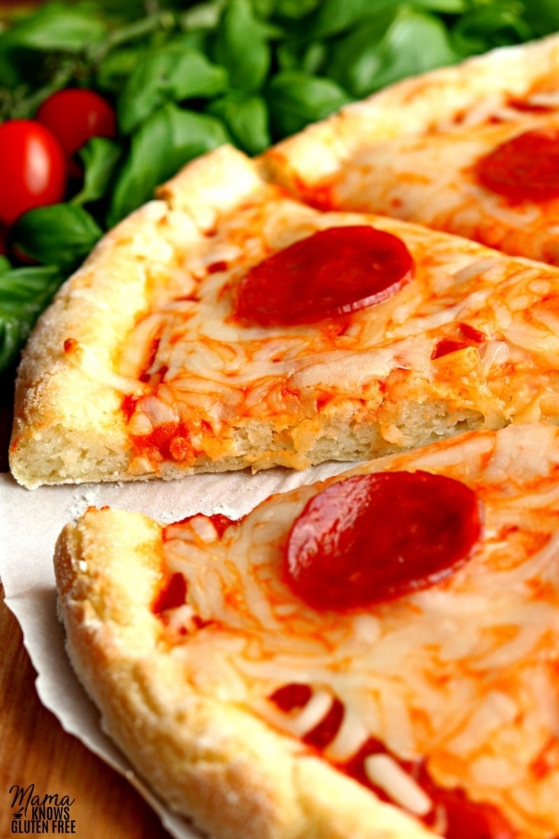 3 slices of gluten-free cheese and pepperoni pizza with basil and tomatoes in the background