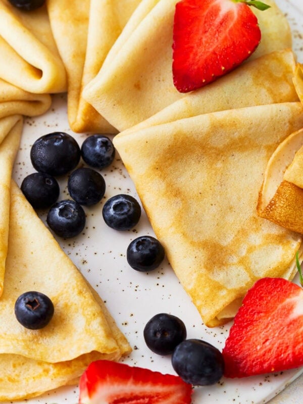 triangles of gluten-free crepes arranged on a platter with fresh fruit.