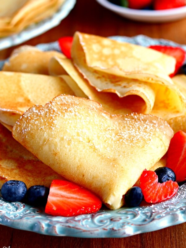 a plate full of folded gluten-free crepes with strawberries and blueberries with crepes and strawberries in the background