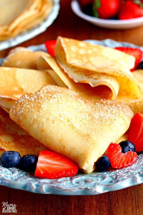 a plate full of folded gluten-free crepes with strawberries and blueberries with crepes and strawberries in the background