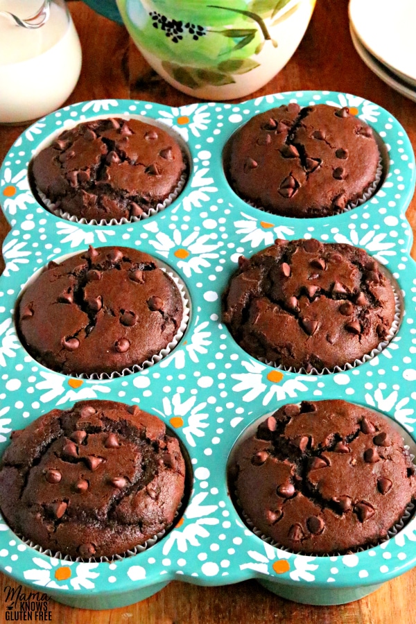 teal muffin pan with 6 gluten-free chocolate muffins with cream, coffee cup and plates in the background