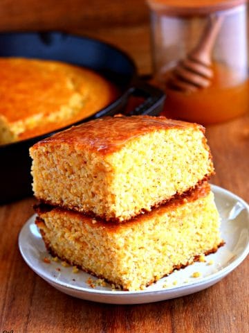 2 pieces of gluten-free cornbread stacked on top of each other with a skittlet of cornbread and honey jar in the background