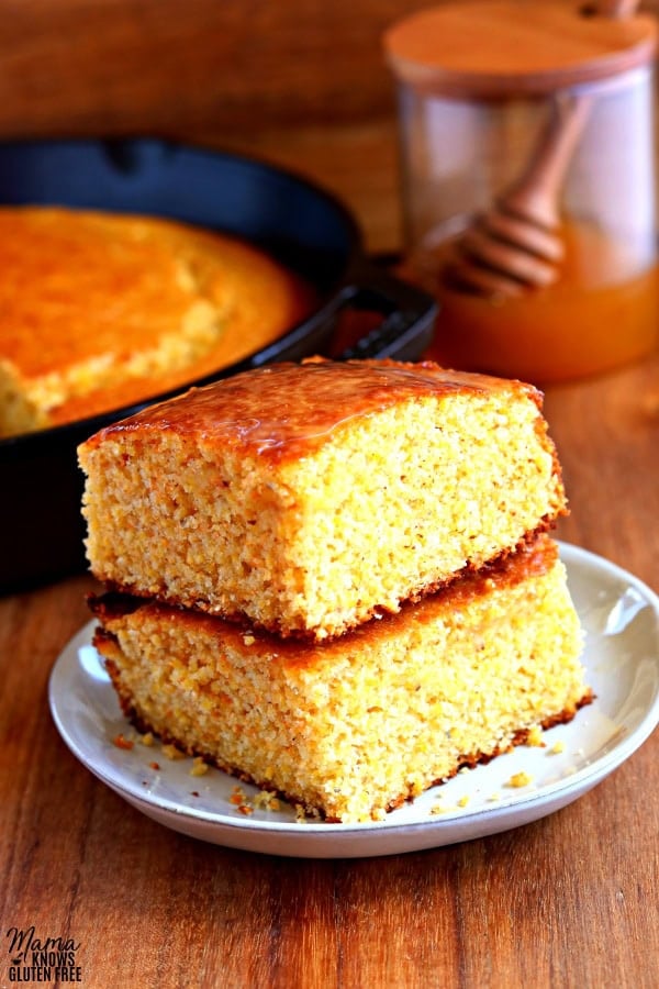 2 pieces of gluten-free cornbread stacked on top of each other with a skittlet of cornbread and honey jar in the background