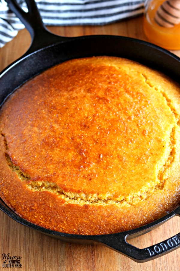 skillet of gltuen-free cornbread with a honey jar and kitchen towel in the background
