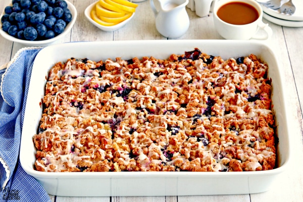 a pan of gluten-free blueberry lemon breakfast casserole with blueberries, lemon, creamer and coffee in the background