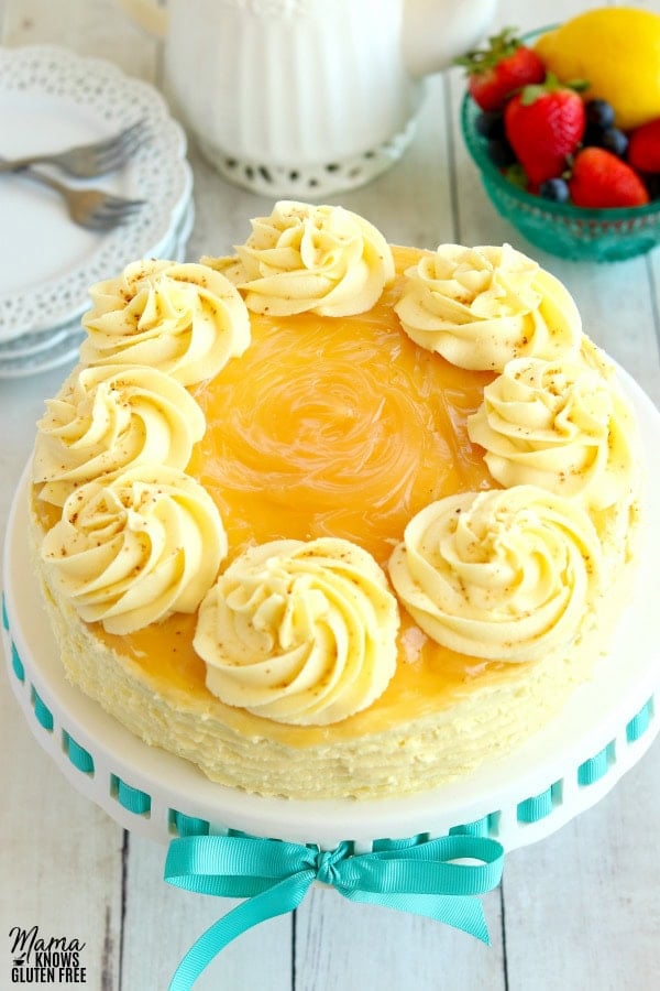 lemon cake with lemon buttercream frosting with berries, lemon, tea pot and plates in the background