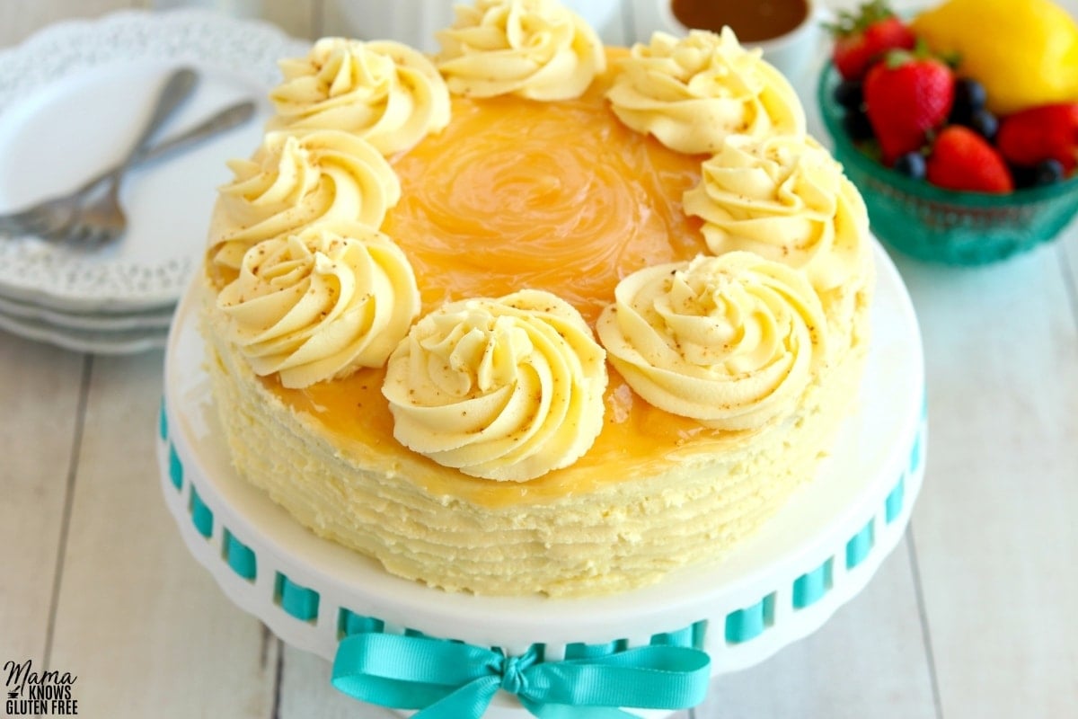 gluten-free lemon cake on a white cake plate with berries and white plates with forks in the background