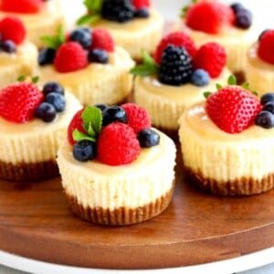 mini cheesecakes topped with berries on a wood platter with berries, graham crackers and coffee in the background