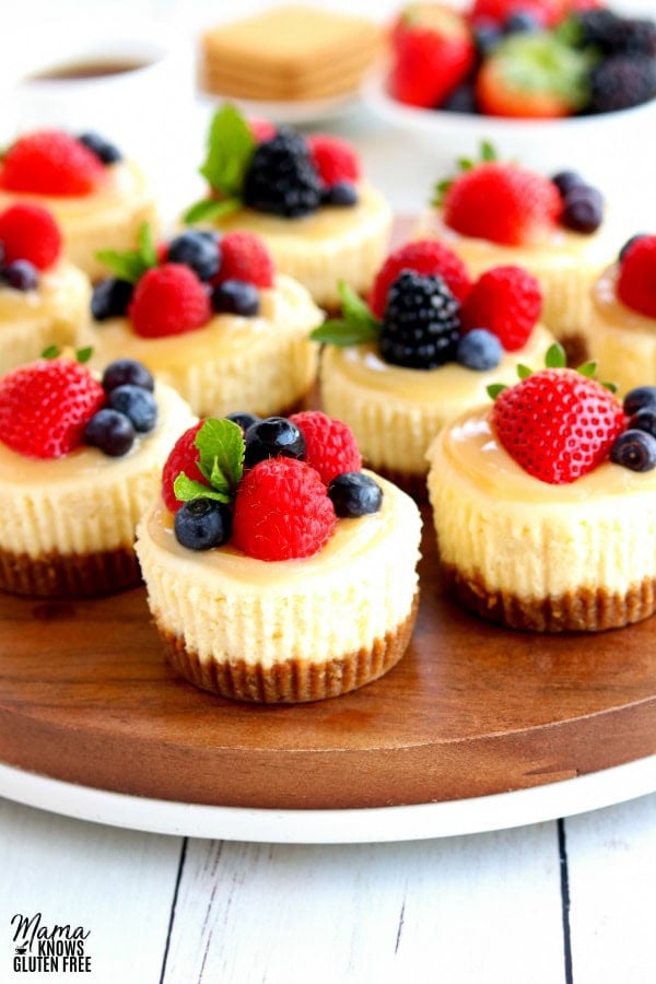 mini cheesecakes topped with berries on a wood platter with berries, graham crackers and coffee in the background