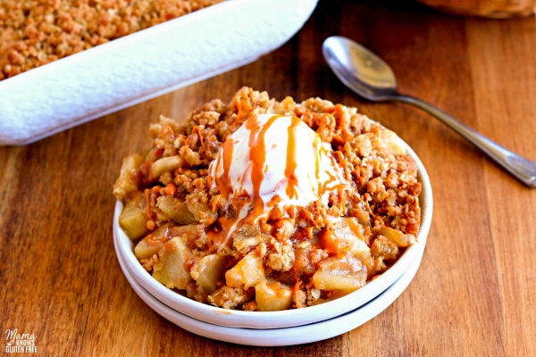 gluten-free apple crisp in a dish with ice cream on top with a pan of apple crisp in the background