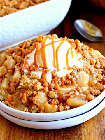 gluten-free apple crisp topped with vanilla ice cream on a white plate with a spoon and crisp in the background