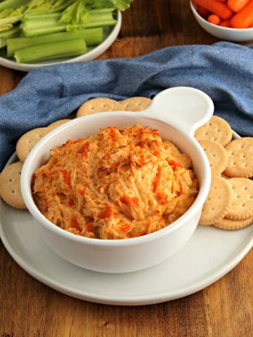bowl of buffalo chicken dip with crackers and celery and carrots in the background