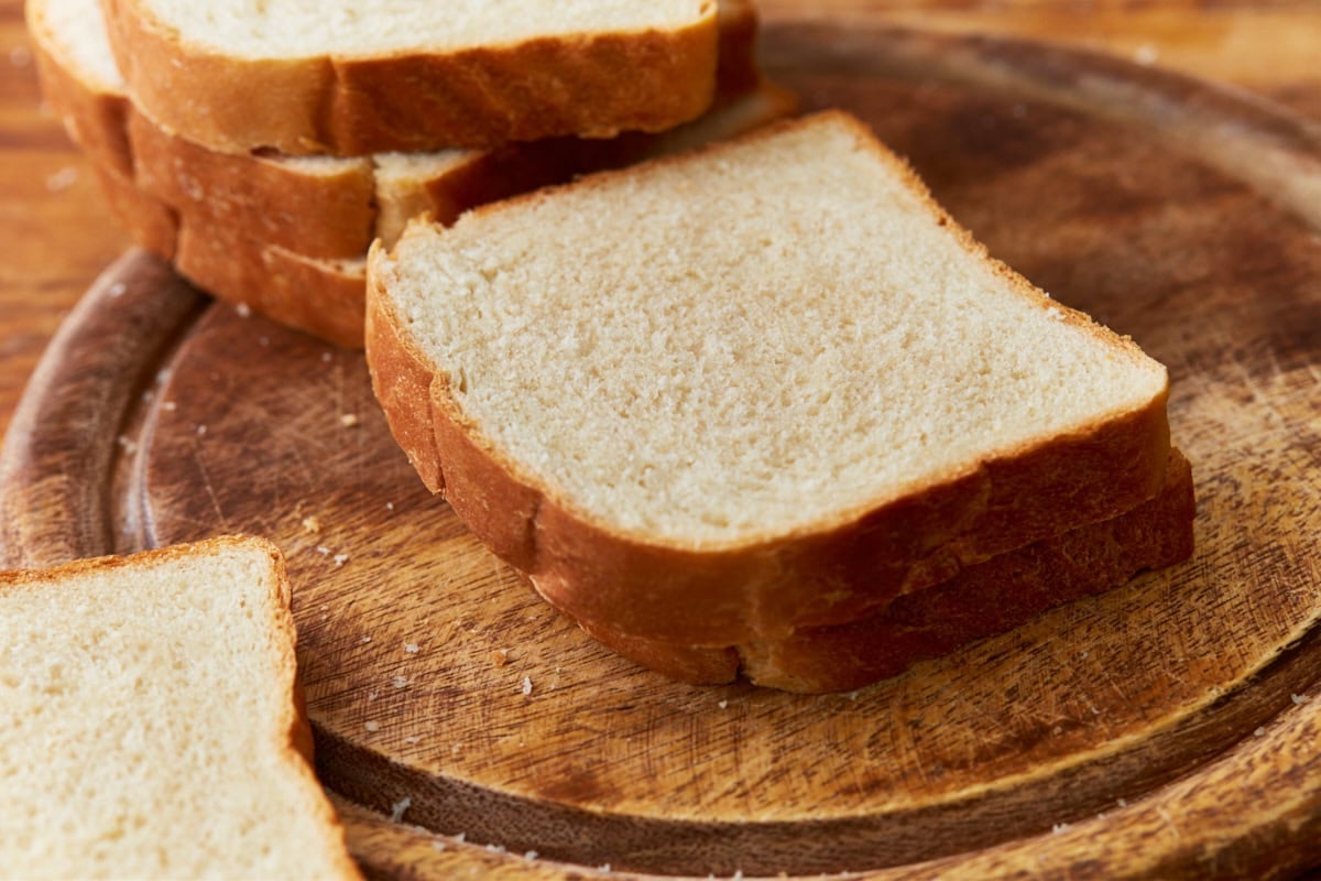 Two pieces of gluten-free dough stack on a wooden cutting board with three pieces stacked behind