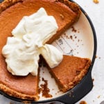 Overhead view of gluten-free pumpkin pie topped with whipped cream, in a pie dish with some slices missing.