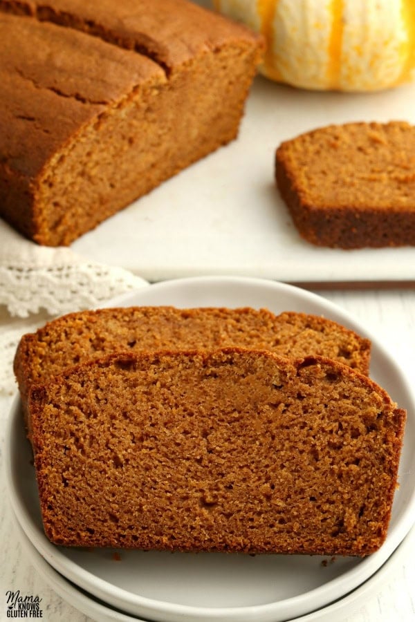 2 slices of gluten-free pumpkin bread on a white plate with the loaf and another slice in the background