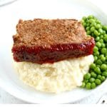 a piece of gluten-free meatloaf on a white plate with mashed potatoes and green peas