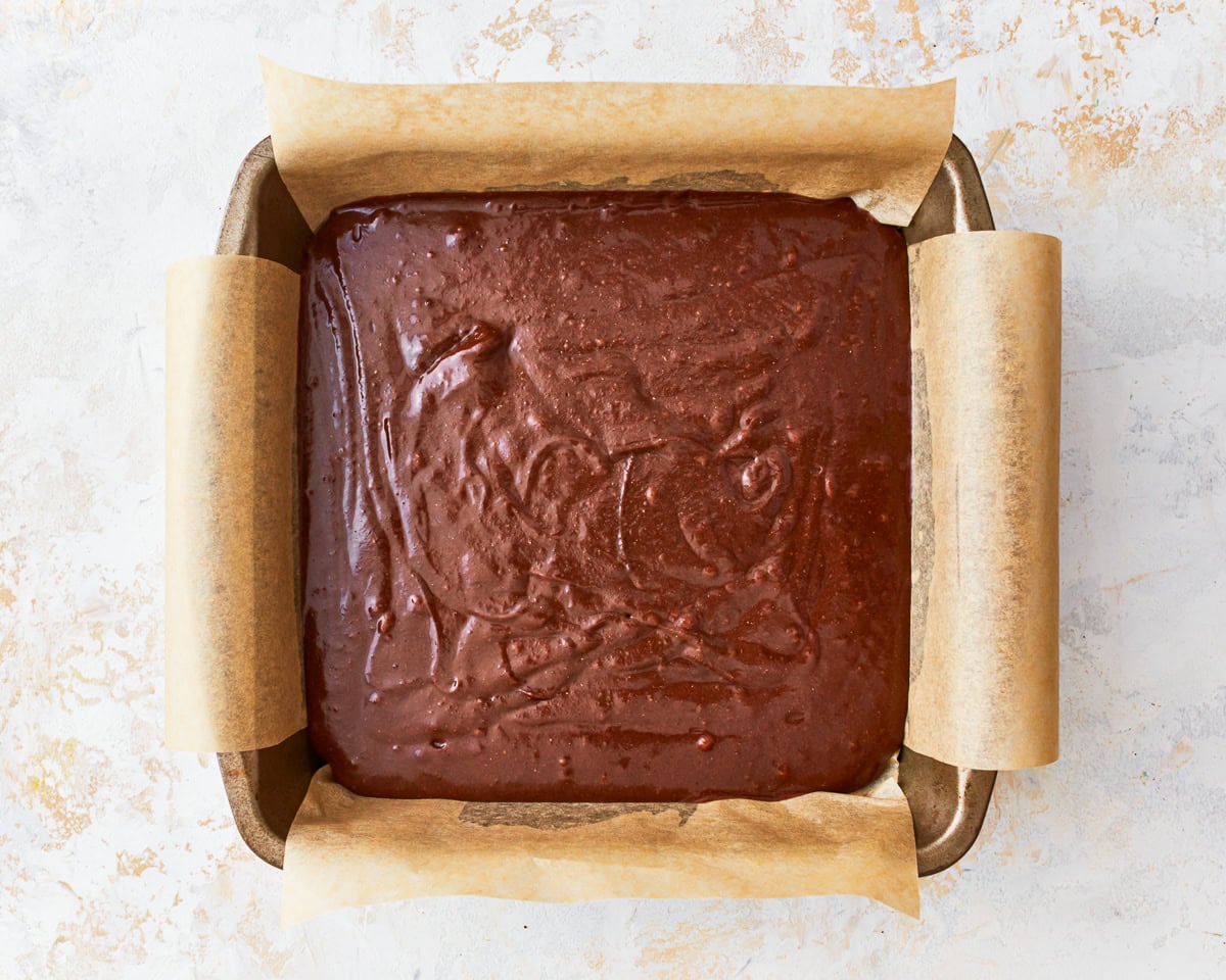 gluten free brownie batter in a lined square baking pan.