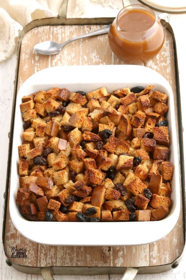 baking dish of gluten-free bread pudding with caramel sauce on a wooden tray