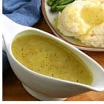 white gravy boat filled with gluten-free gravy wiht a plated of mashed potatoes and green beans in the background