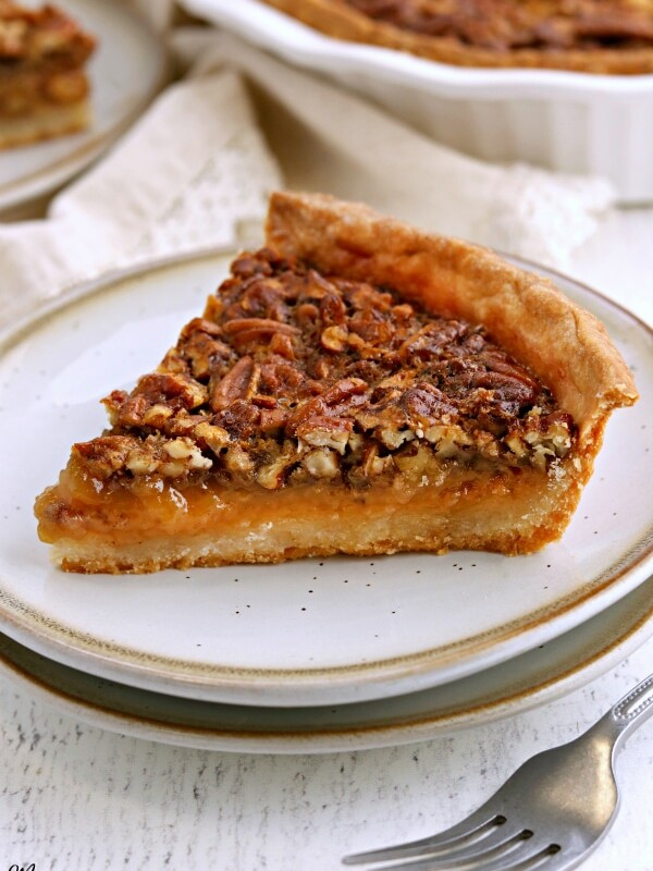 slice of gluten-free pecan pie on a white plate with a fork and the pie in the background