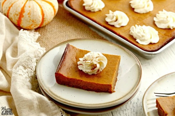 two gluten-free pumpkin pie bars on plates with the bars and pumpkins in the backgorund