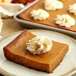 slice of gluten-free pumpkin pie bar on plate with pan of bars in the background