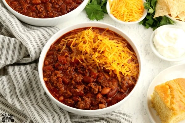 bowl of gluten-free chili with cornbread and chili toppings in the background