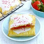 two gluten-free pop-tarts stacked on top of eachother on a blue plate with pop tarts and strawberries in the background