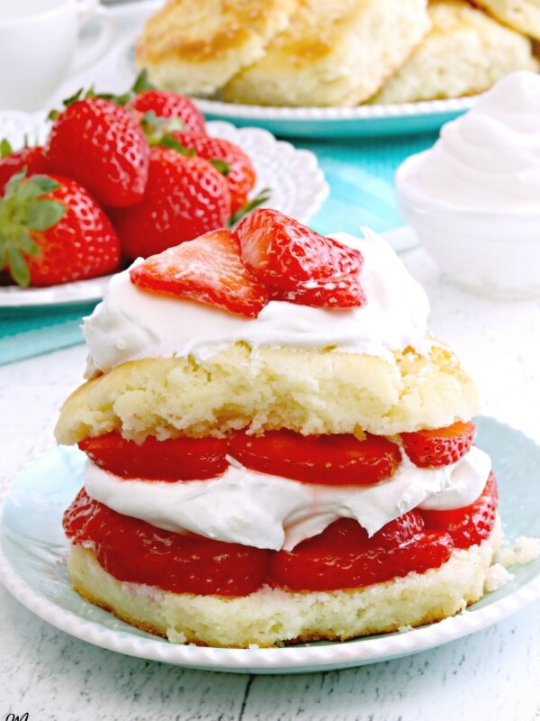 gluten-free strawberry shortcake on blue plate with strawberries, whipped cream, and plate of short cakes in the background