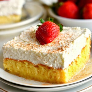 slice of gluten-free Tres Leches Cake with the cake and strawberries in the background