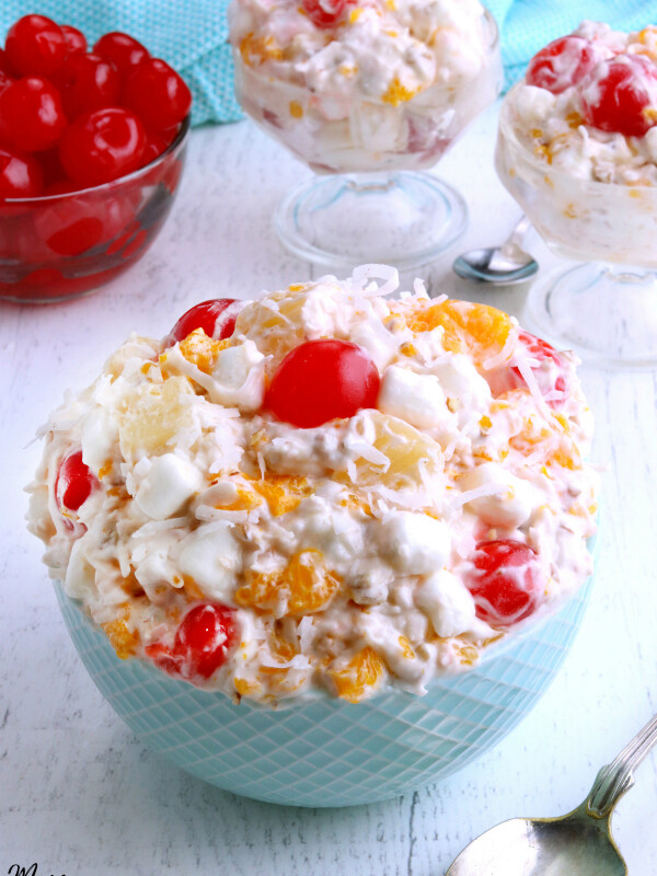 ambrosia salad in a bowl with cherries and two servings in the background