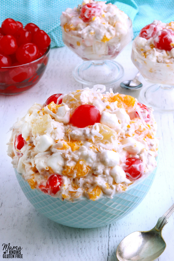 ambrosia salad in a bowl with cherries and two servings in the background