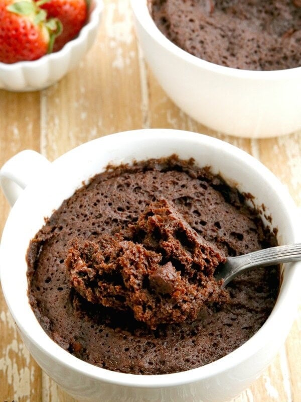 gluten-free chocolate mug cake wth spoon and anotehr cake and strawberries in the background