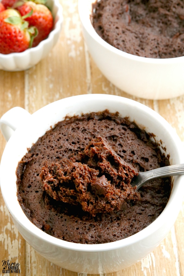 gluten-free chocolate mug cake wth spoon and anotehr cake and strawberries in the background